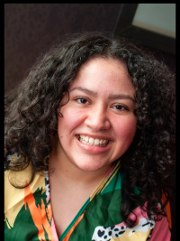 Woman with curly dark brown hair in a brightly colored dress 0